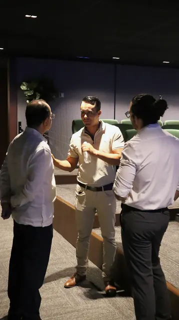 Tres asistentes conversando de pie entre las butacas del auditorio, antes de que empiece la sesión.